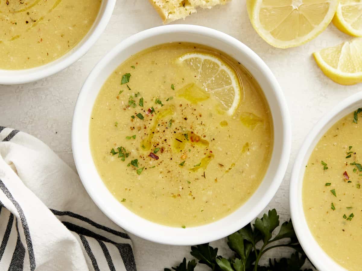 Overhead view of three bowls of lemony chickpea soup garnished with slices of lemon.