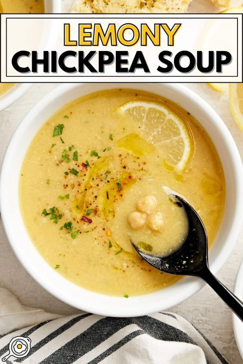 Overhead view of a bowl of lemony chickpea soup with a black spoon and slice of lemon.