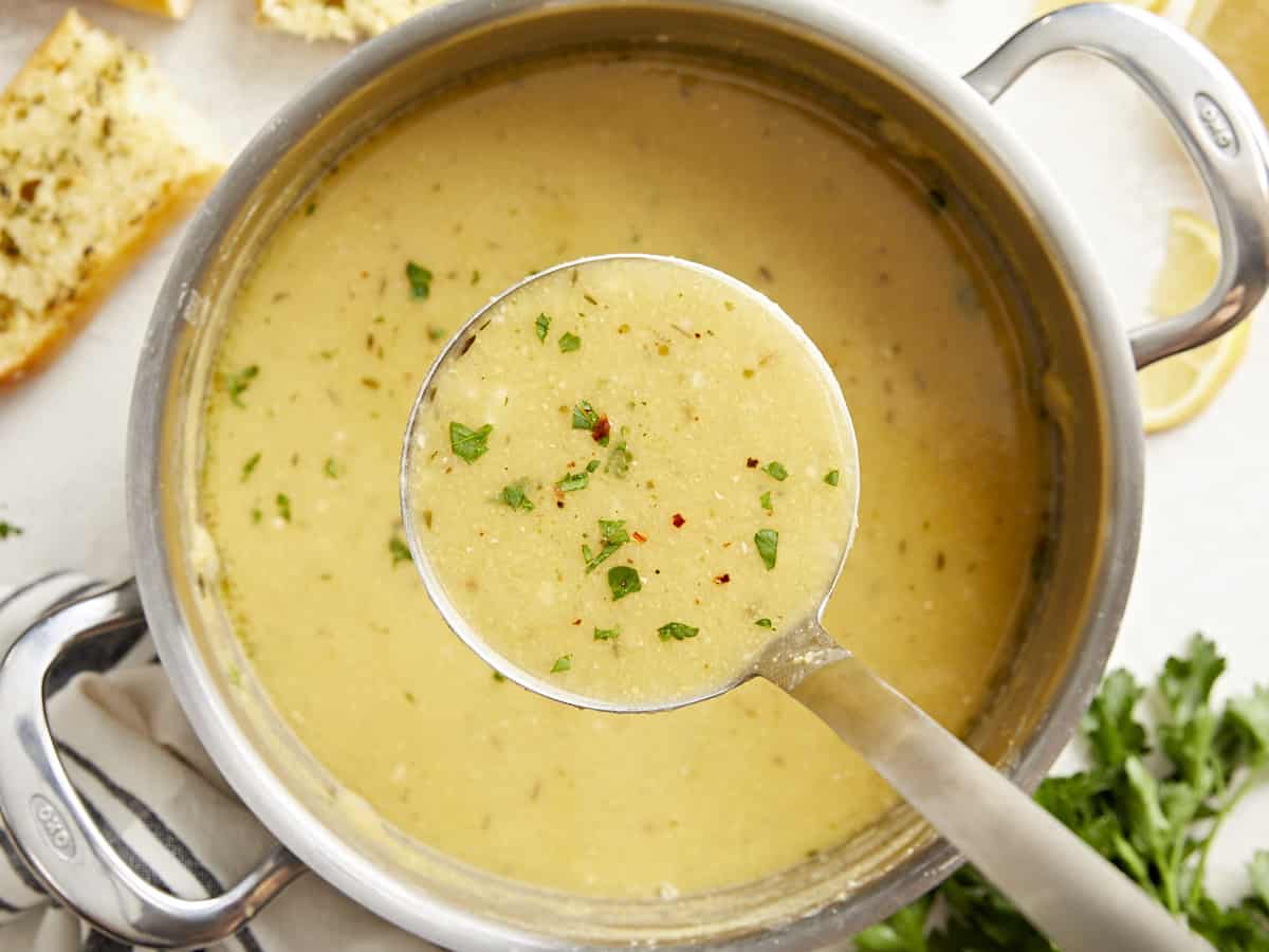 A ladle full of lemony chickpea soup held close to the camera over the pot of soup.