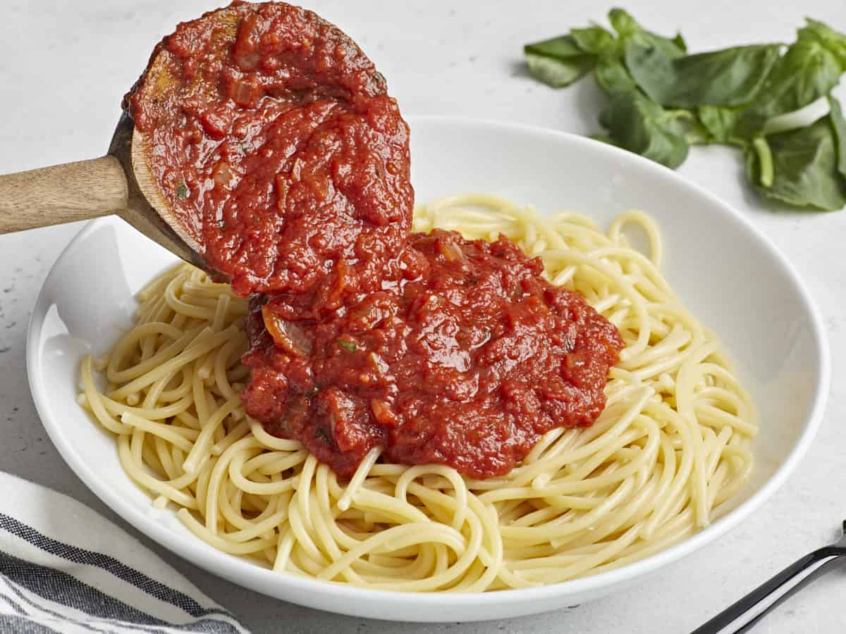 Marinara sauce being spooned over a plate of pasta.