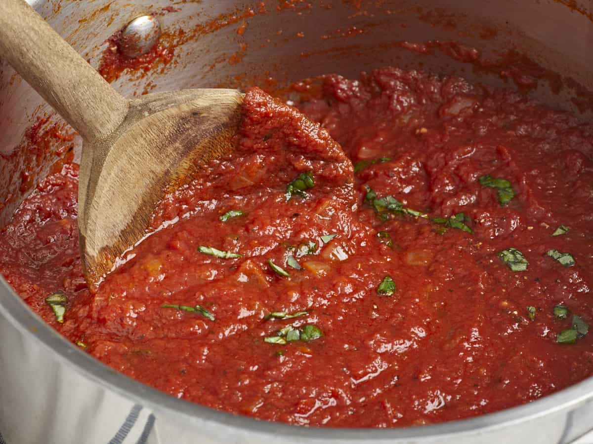 Close up side view of marinara sauce being stirred in the pot with a wooden spoon.