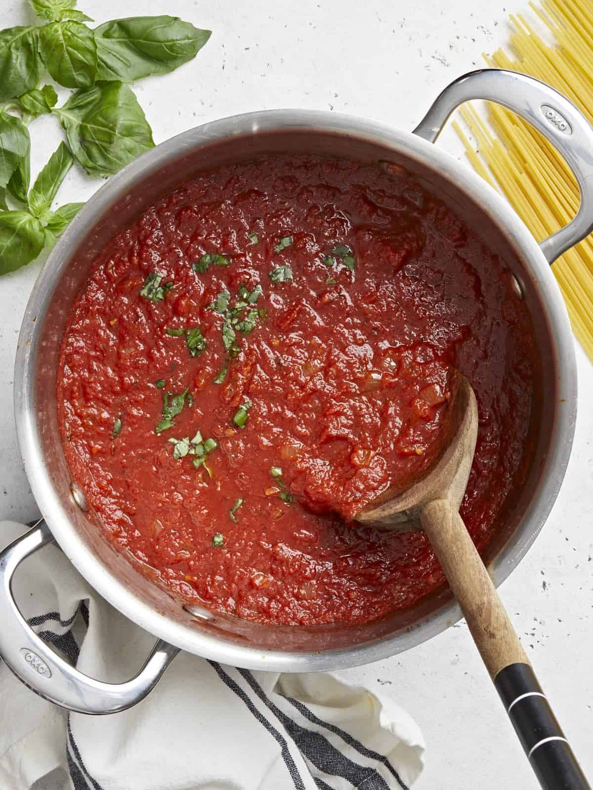 Overhead view of a pot full of homemade marinara sauce with a wooden spoon in the center.