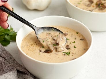 Side view of a bowl of creamy mushroom soup with a spoon lifting some out of the bowl.