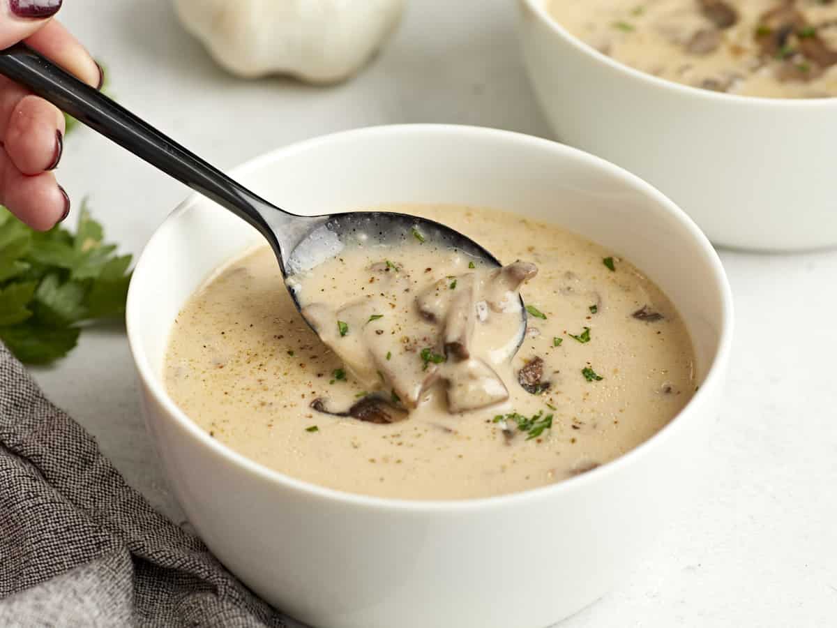 Side view of a bowl of creamy mushroom soup with a spoon lifting some out of the bowl.