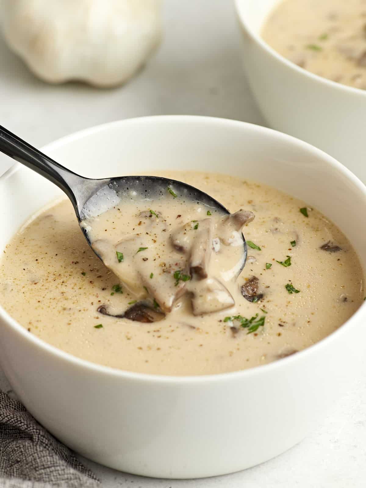 Side view of a bowl of creamy mushroom soup with a spoon lifting some out of the bowl.