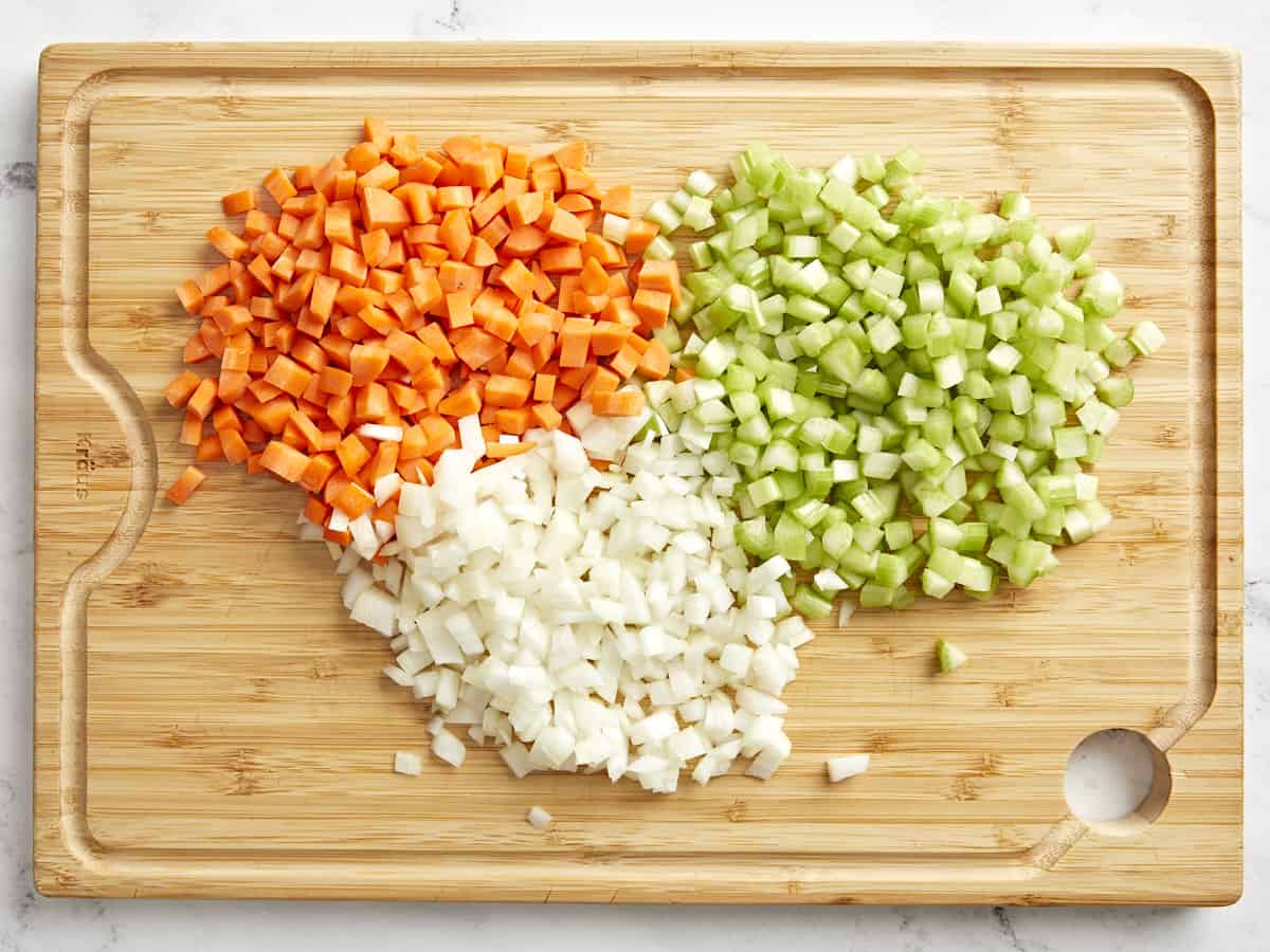 finely diced onion, carrot, and celery on a bamboo cutting board.