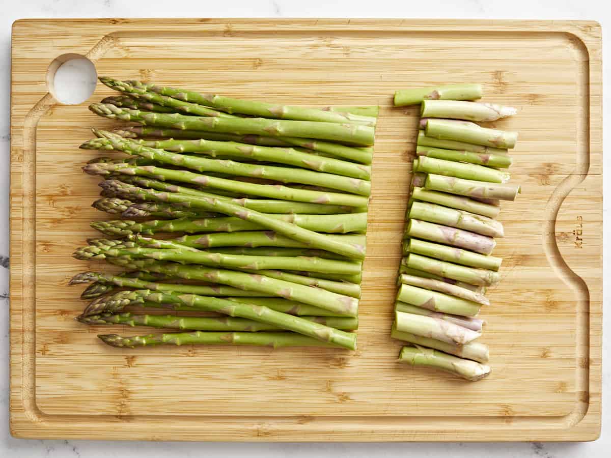 a bunch of asparagus with the ends trimmed off on a bamboo cutting board.