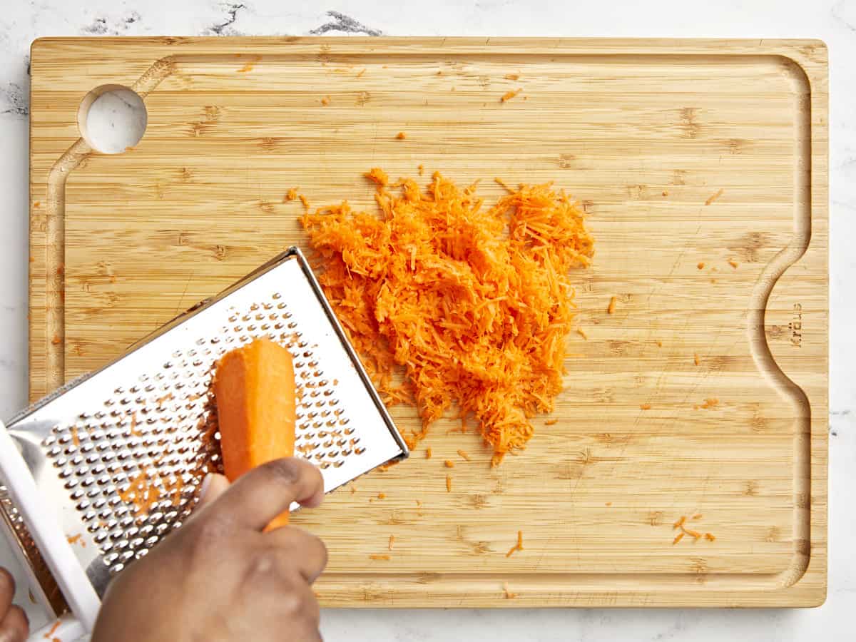 A carrot being grated on a wood cutting board.