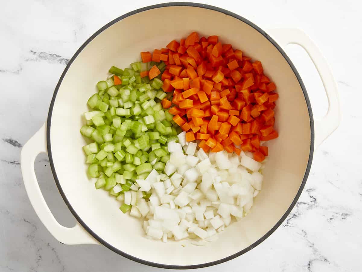 Chopped celery, carrots and onions in a white Dutch oven.