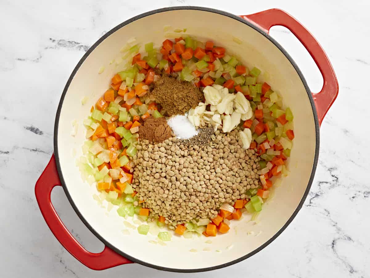Mirepoix, spices and lentils in a red casserole dish.