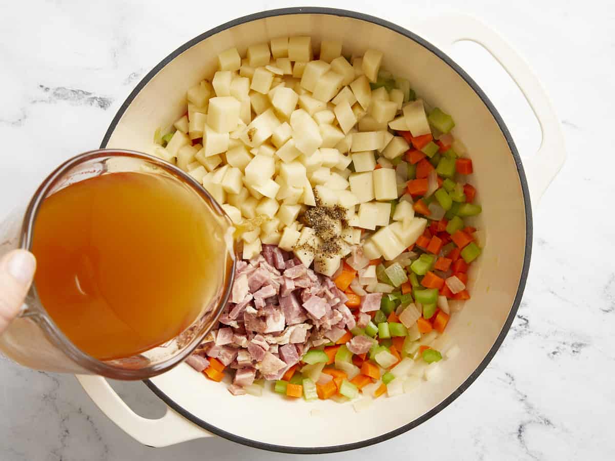 broth poured over mirepoix, potatoes, and ham in a dutch oven.