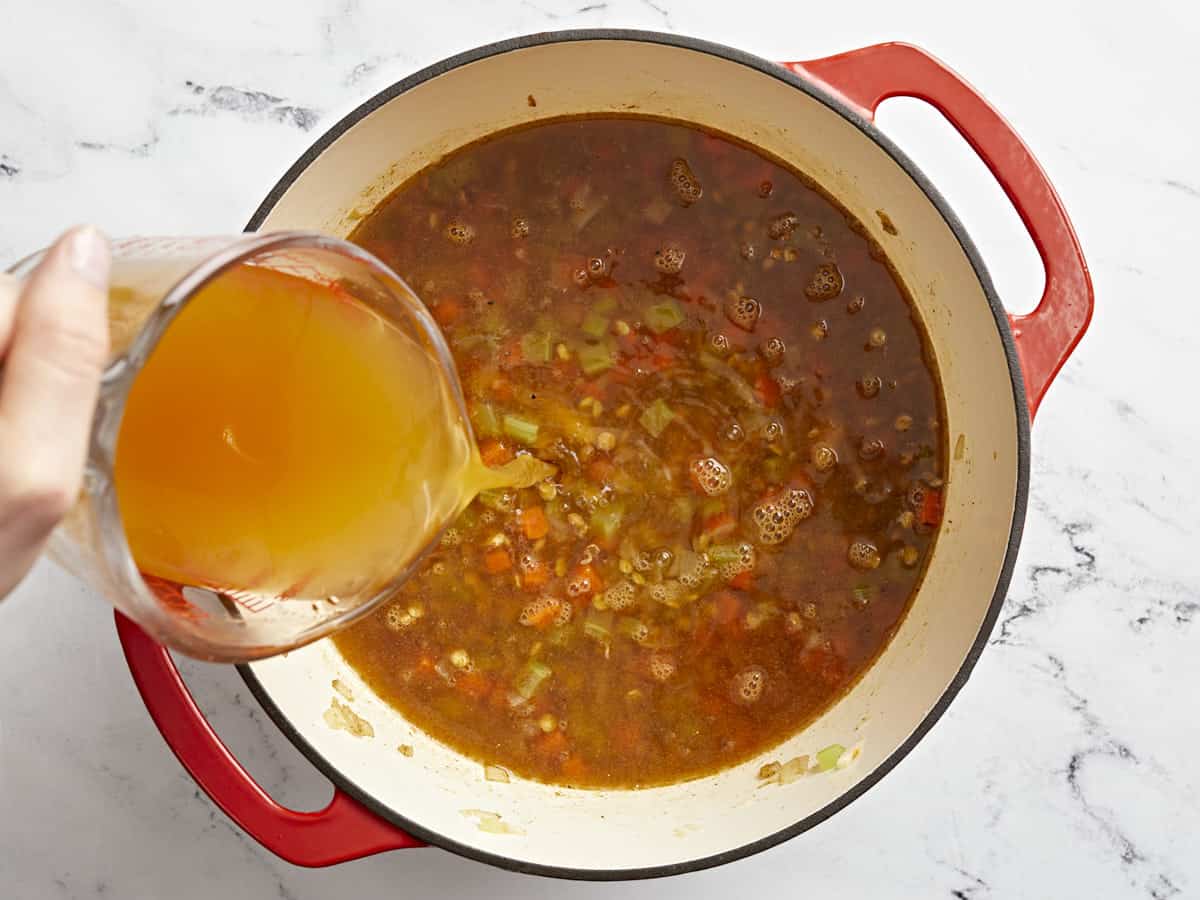 broth added to lentil soup in a red dutch oven.