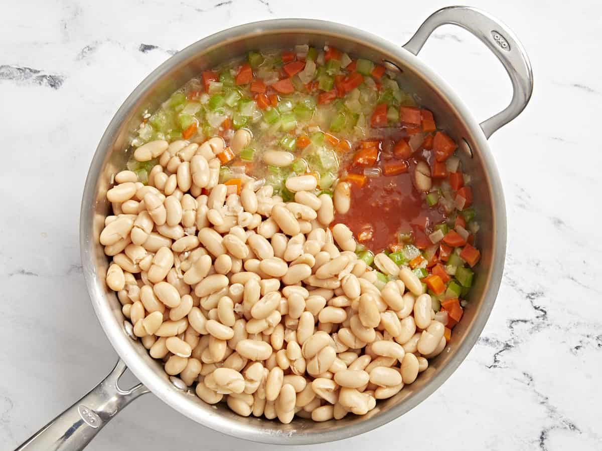 Add cannellini beans and buffalo sauce to sautéed vegetables in a skillet.