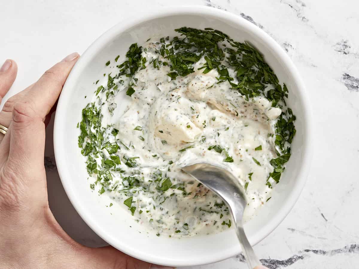 stirred mayonnaise dressing with herbs in a white bowl.
