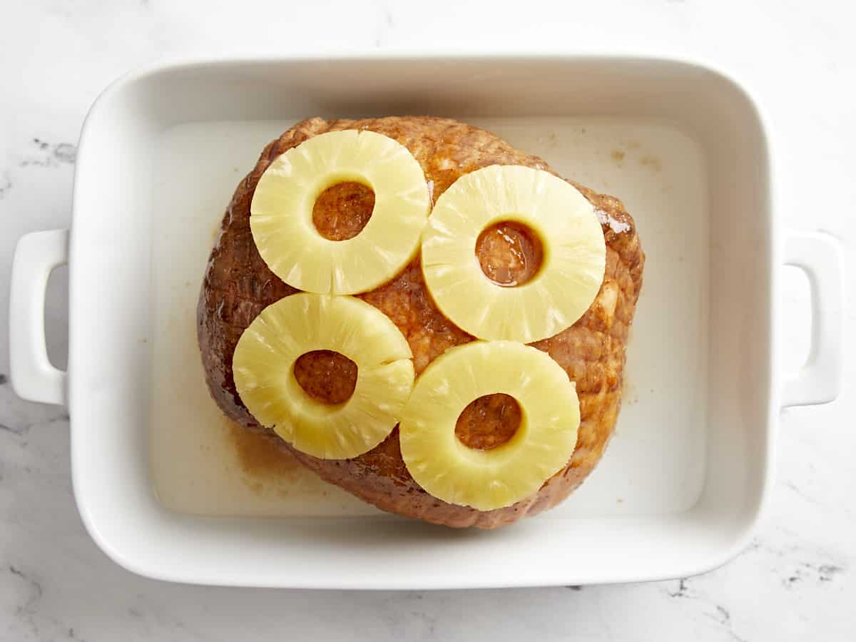 Pineapple rings on a glazed ham in a baking dish.