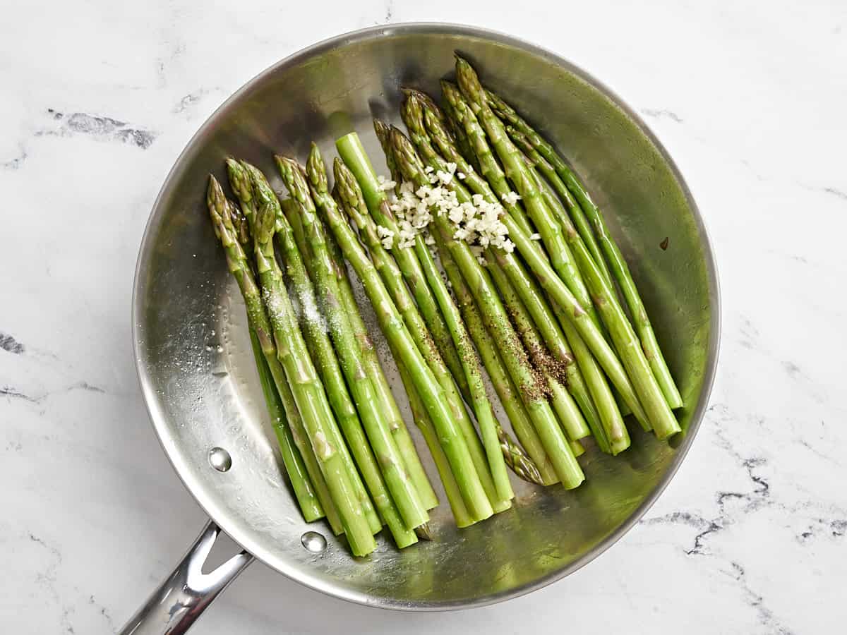 minced garlic on top of asparagus in a frying pan.