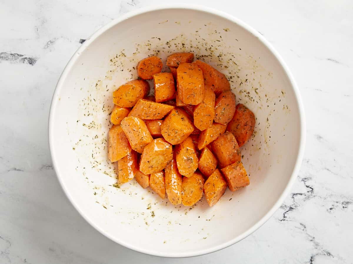 Carrots mixed with butter and dill seasoning in a bowl.