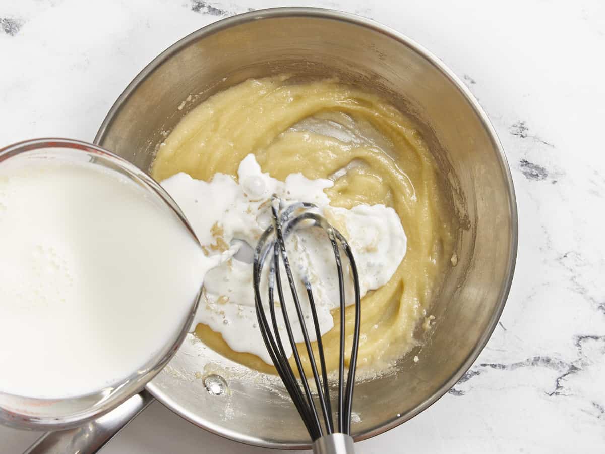 milk poured over butter and flour paste in a frying pan with a whisk.