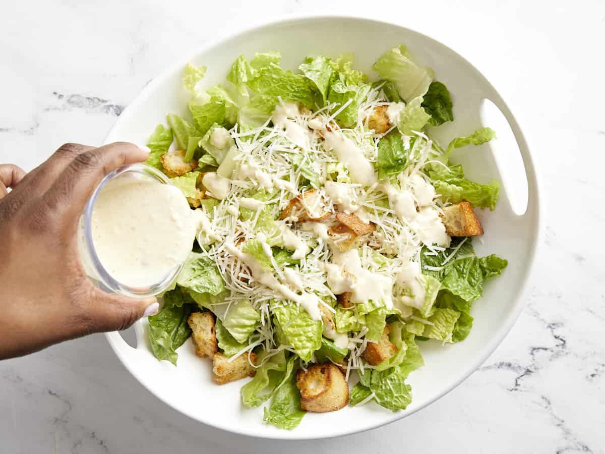 Romaine lettuce, parmesan cheese, croutons, and Caesar dressing added to a serving bowl.