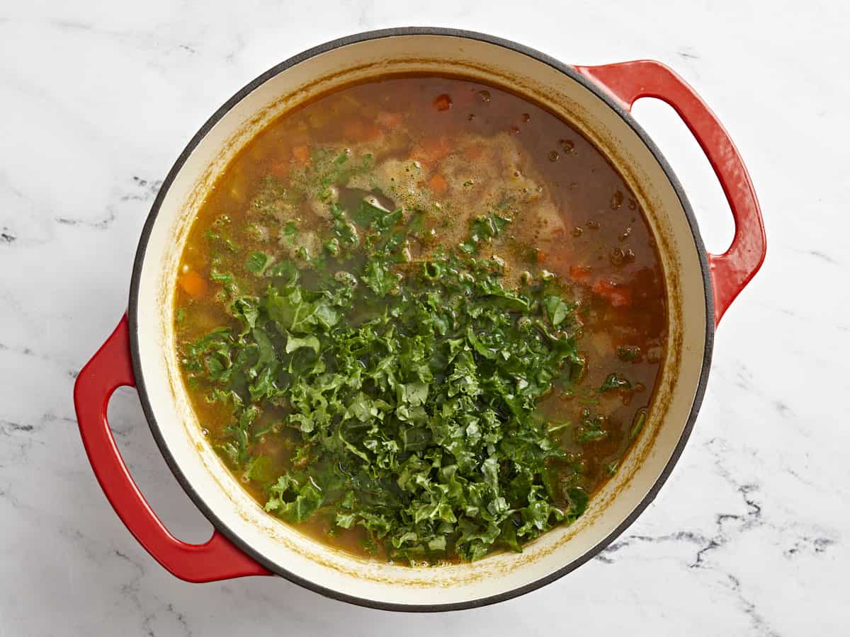 Kale added to lentil soup in a red Dutch oven.