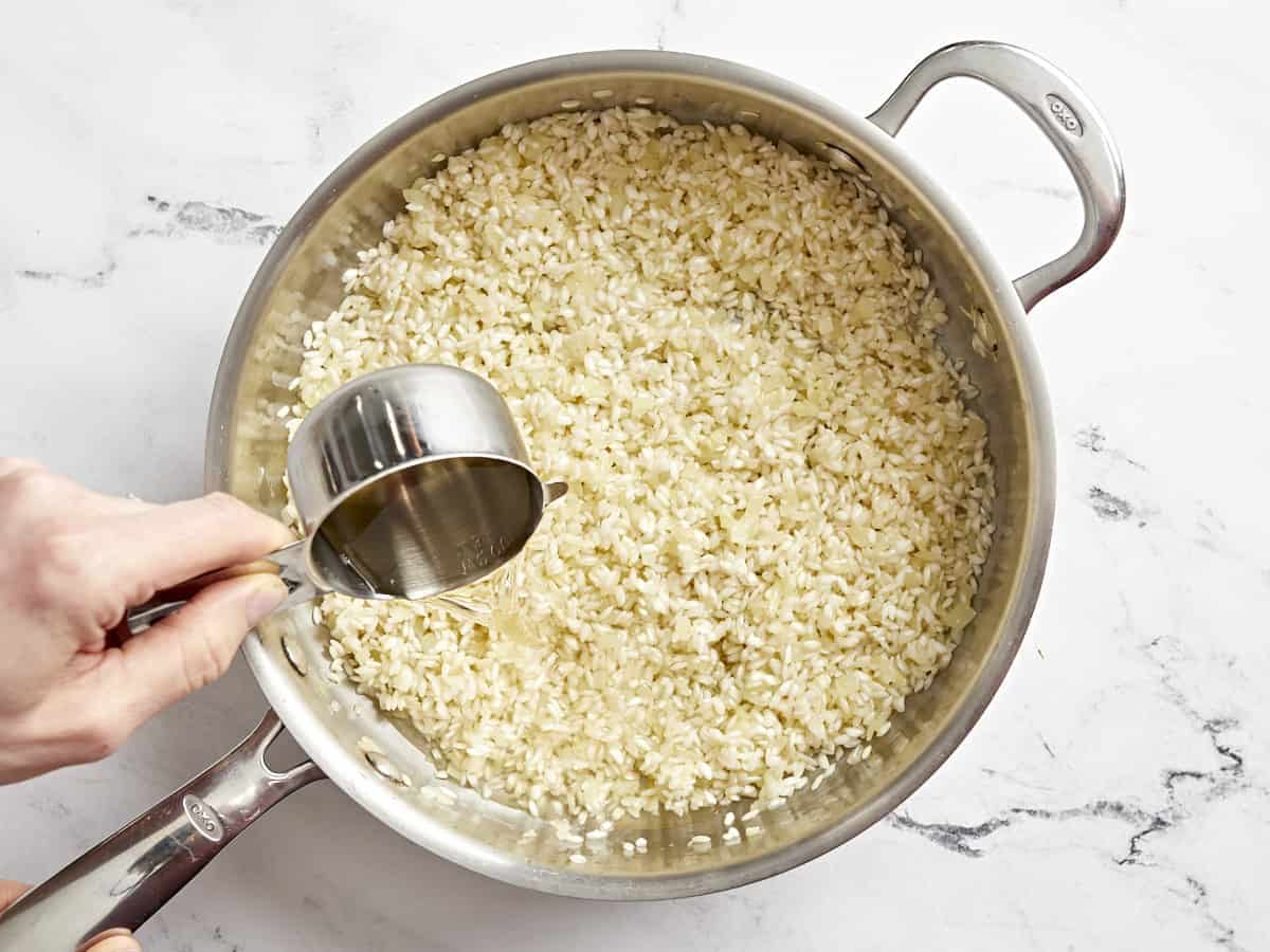 white wine poured over rice and onions in a pan.