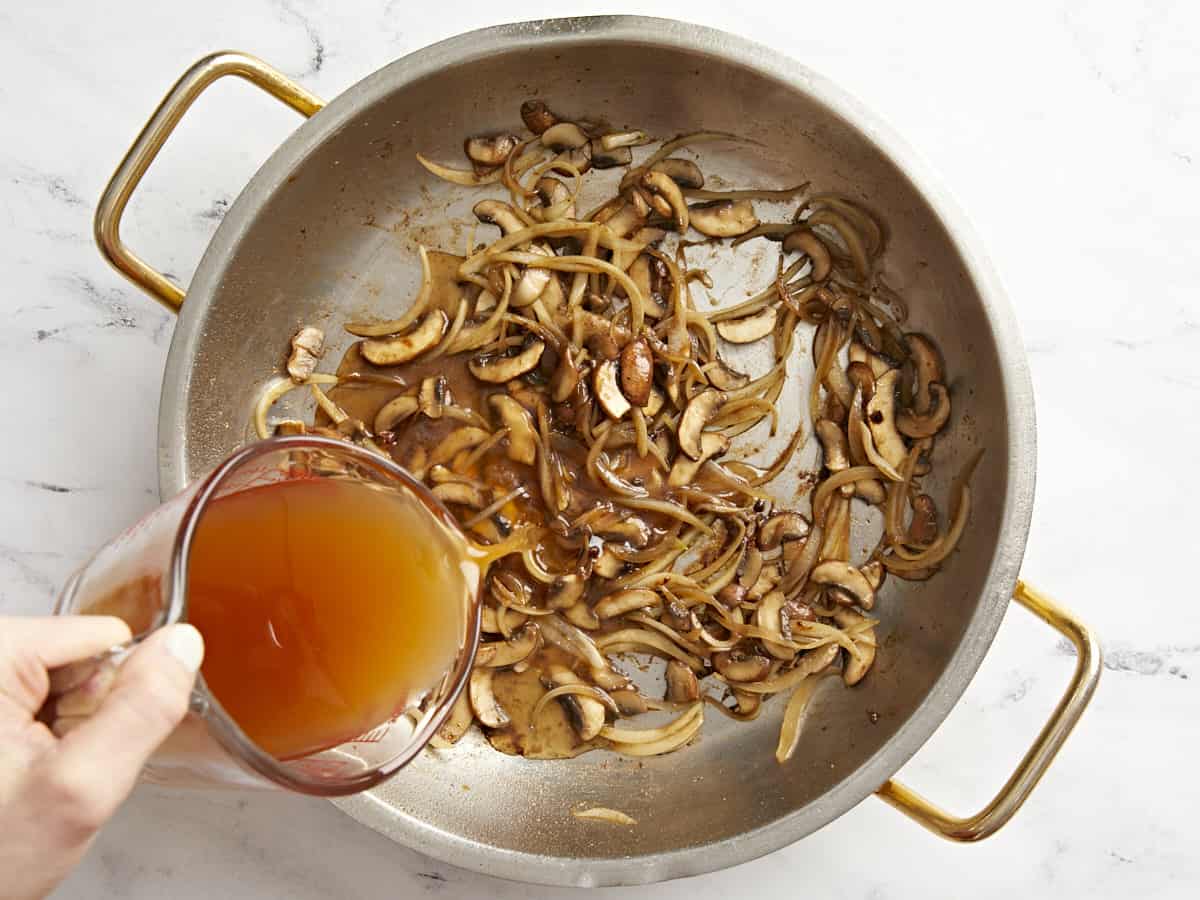 marsala wine poured over mushrooms and onions in a pan.