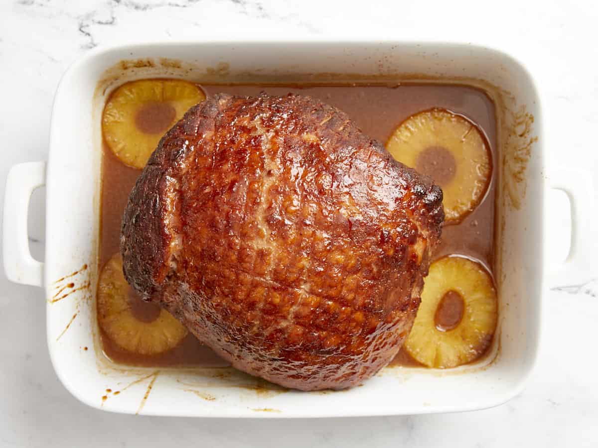 Baked ham in a white baking dish surrounded by pineapple rings.