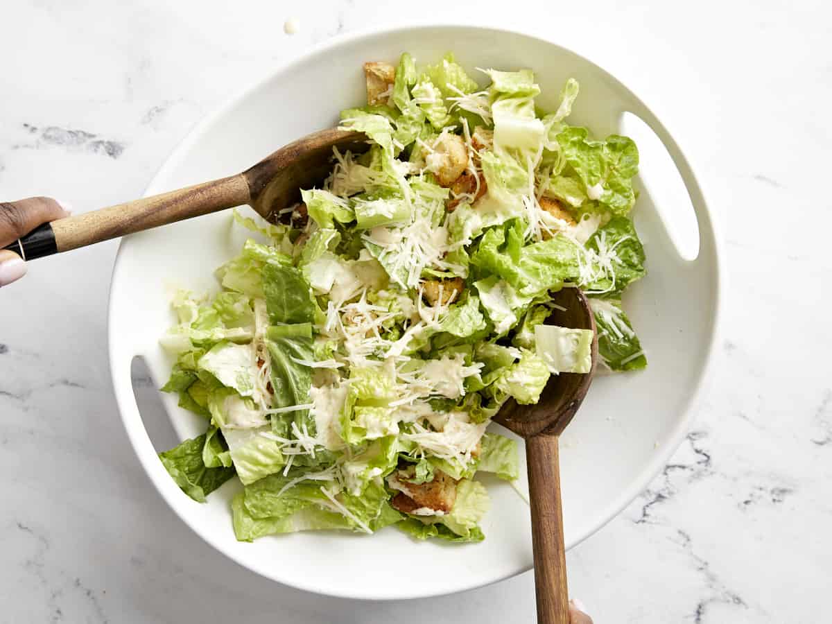 Caesar salad being tossed in a serving bowl.