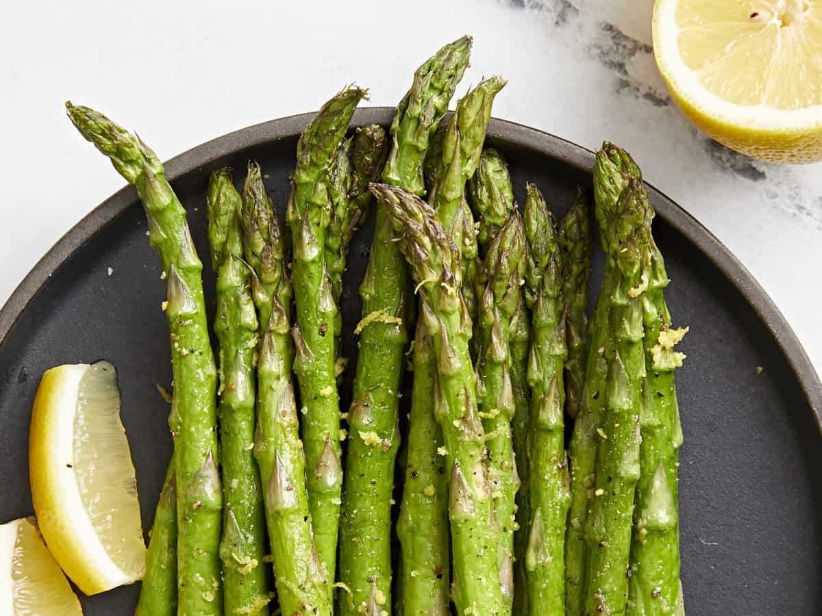 close-up view of asparagus tips on a black plate with lemon wedges.