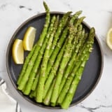 overhead view of asparagus on a black plate with lemon wedges.