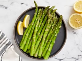 overhead view of asparagus on a black plate with lemon wedges.