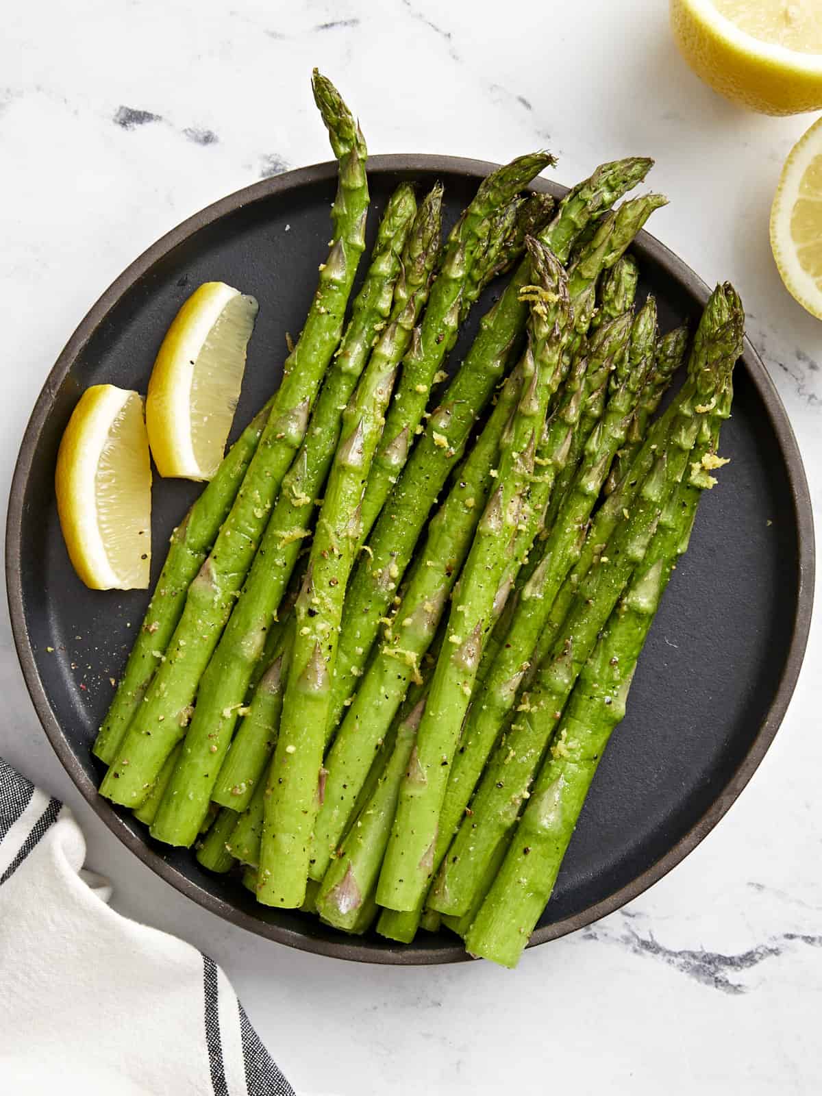 overhead view of asparagus on a black plate with lemon wedges.