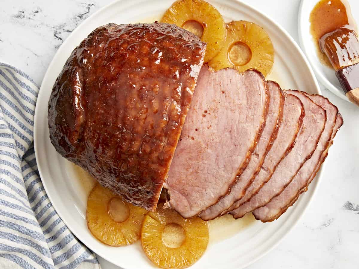 Top view of a partially sliced ​​baked ham on a white plate with pineapple rings.
