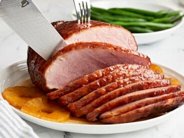 slicing a baked ham on a white plate with pineapple rings.
