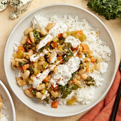 overhead view of buffalo beans and greens over white rice on a white plate with white sauce drizzled over top.