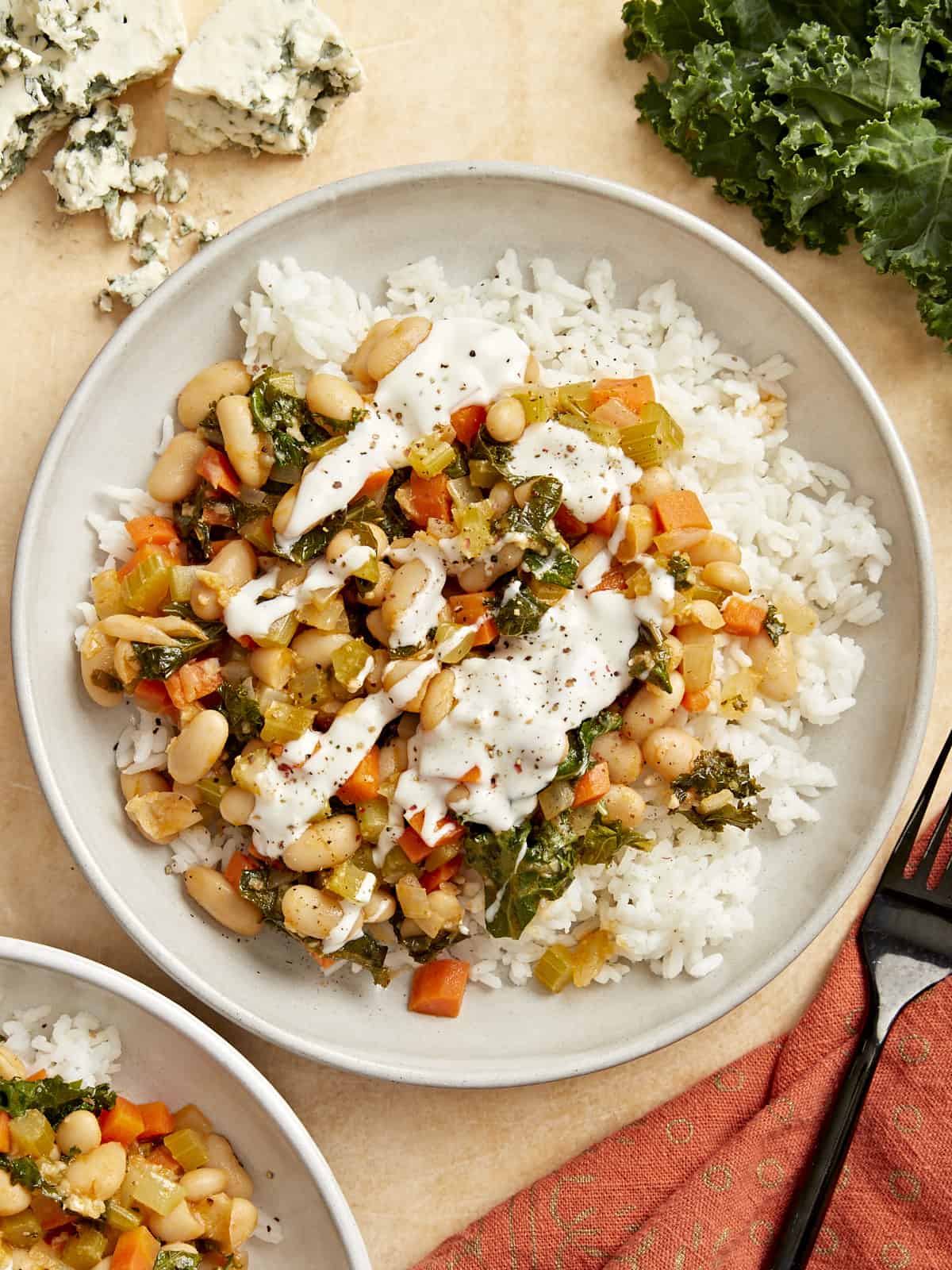 overhead view of buffalo beans and greens over white rice on a white plate with white sauce drizzled over top.