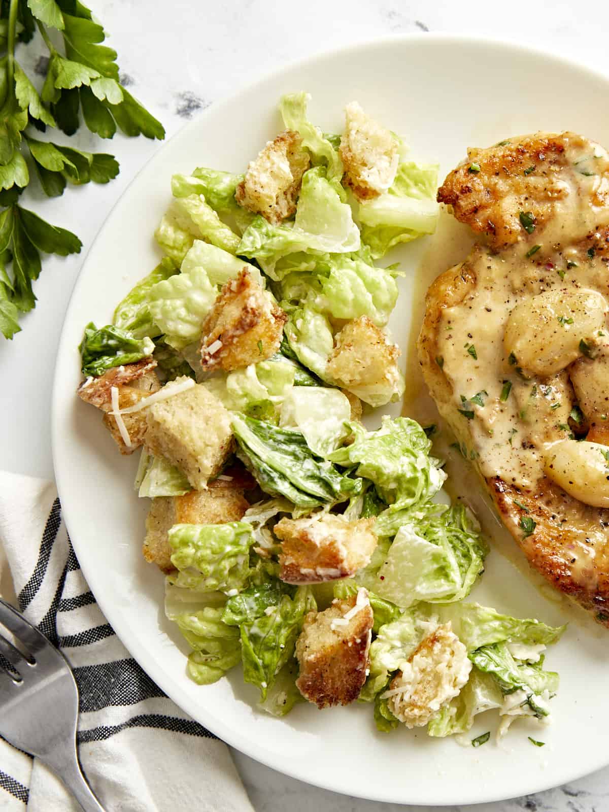 Overhead view of Caesar salad plated with creamy garlic chicken.