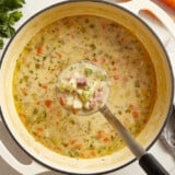 a ladleful of ham and potato soup suspended over a pot of soup.