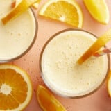 Overhead view of two glasses of orange julius with straws and orange slices.