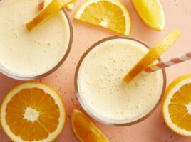 Overhead view of two glasses of orange julius with straws and orange slices.