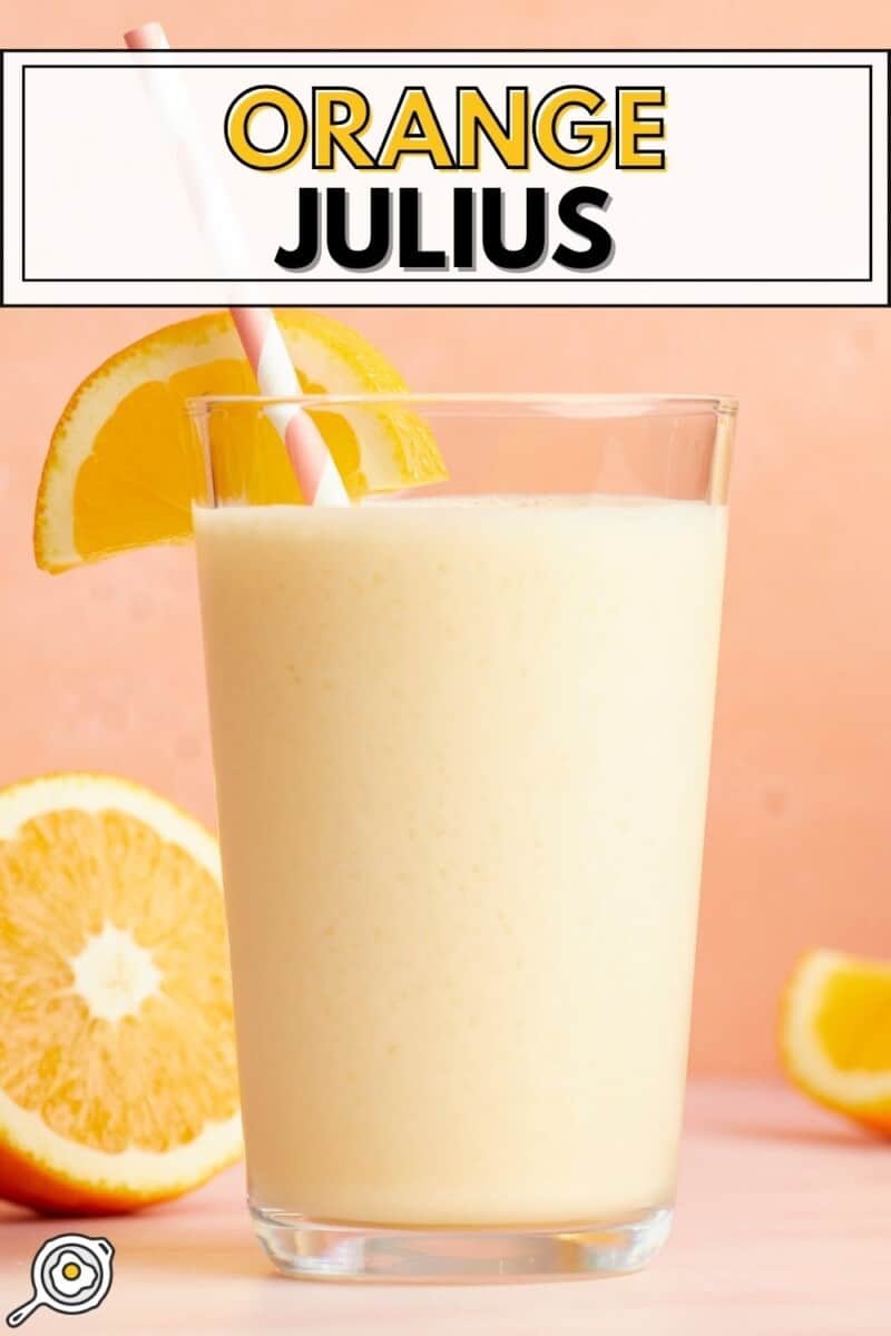 Side view of a tall glass full of Orange Julius with a straw and orange slices.