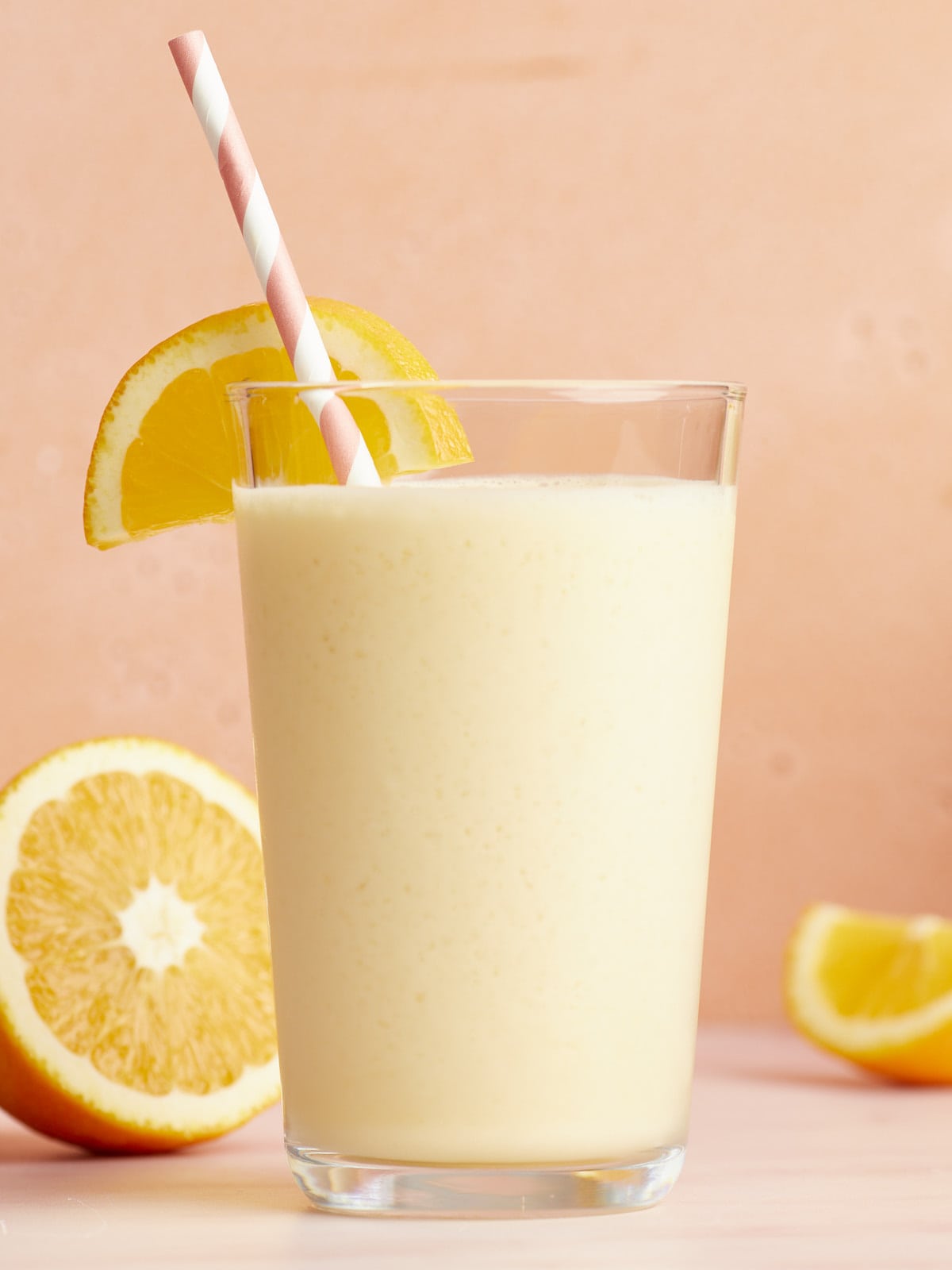Side view of an Orange Julius in a glass with a striped straw and orange slices.