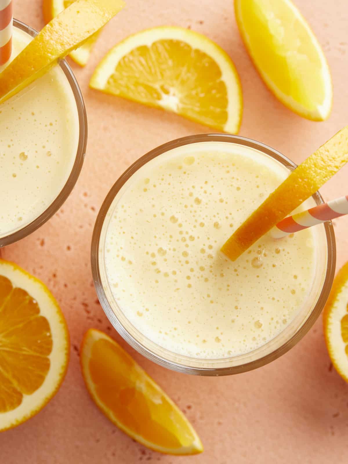 Top view of two glasses full of orange juilius with straws and orange slices.