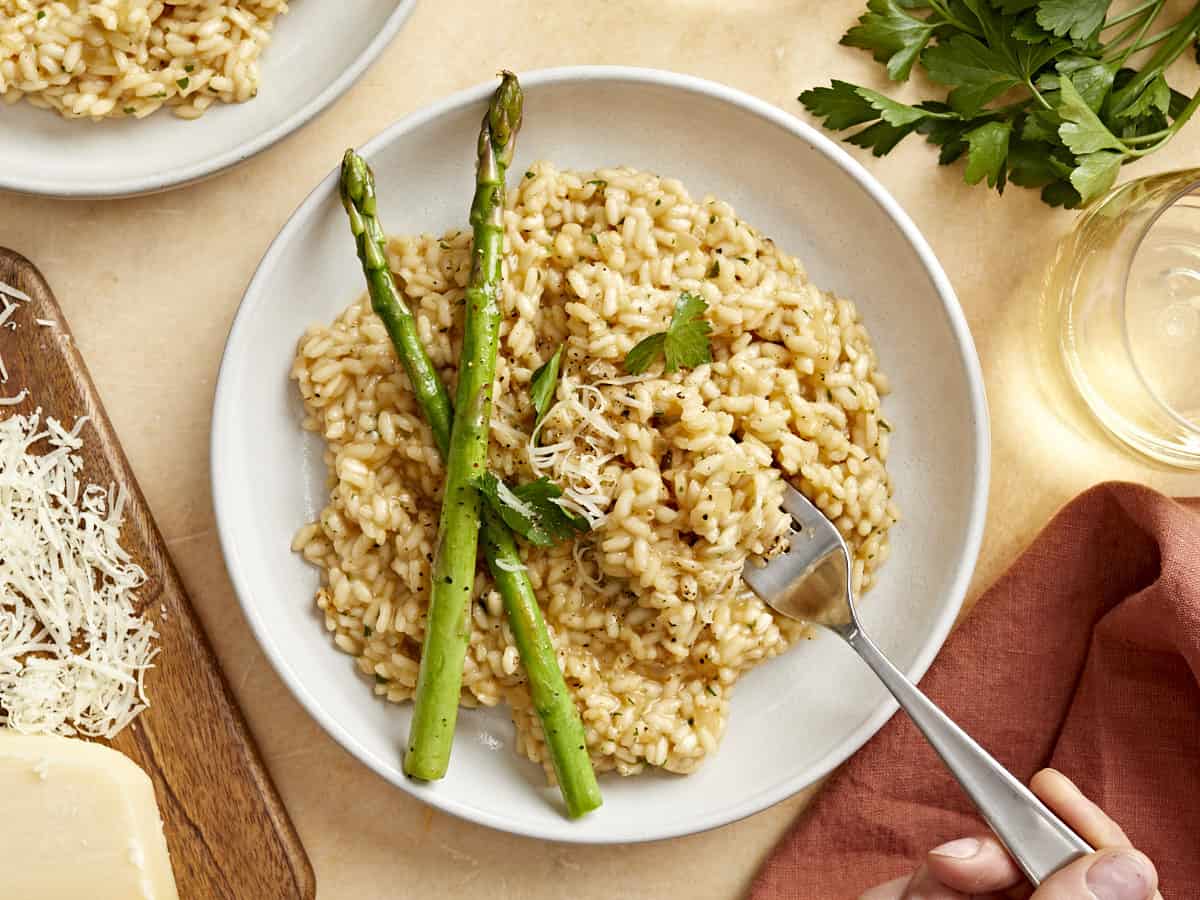 overhead view of parmesan risotto on a white plate with asparagus spears and a fork.
