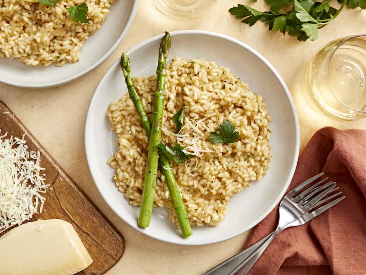 overhead view of parmesan risotto in a white bowl with asparagus spears.