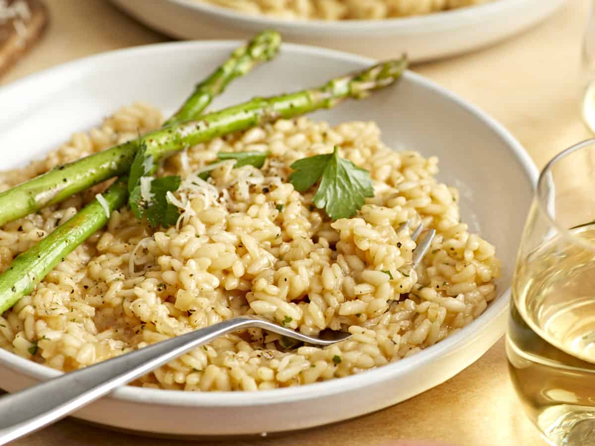 three-quarters view of parmesan risotto in a white bowl with asparagus spears and a fork.