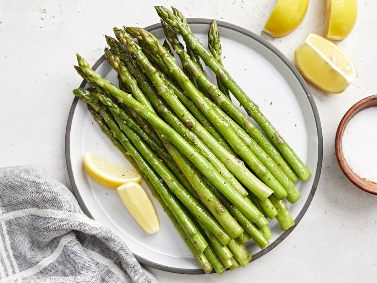 overhead view of sauteed asparagus on a plate with lemon wedges.