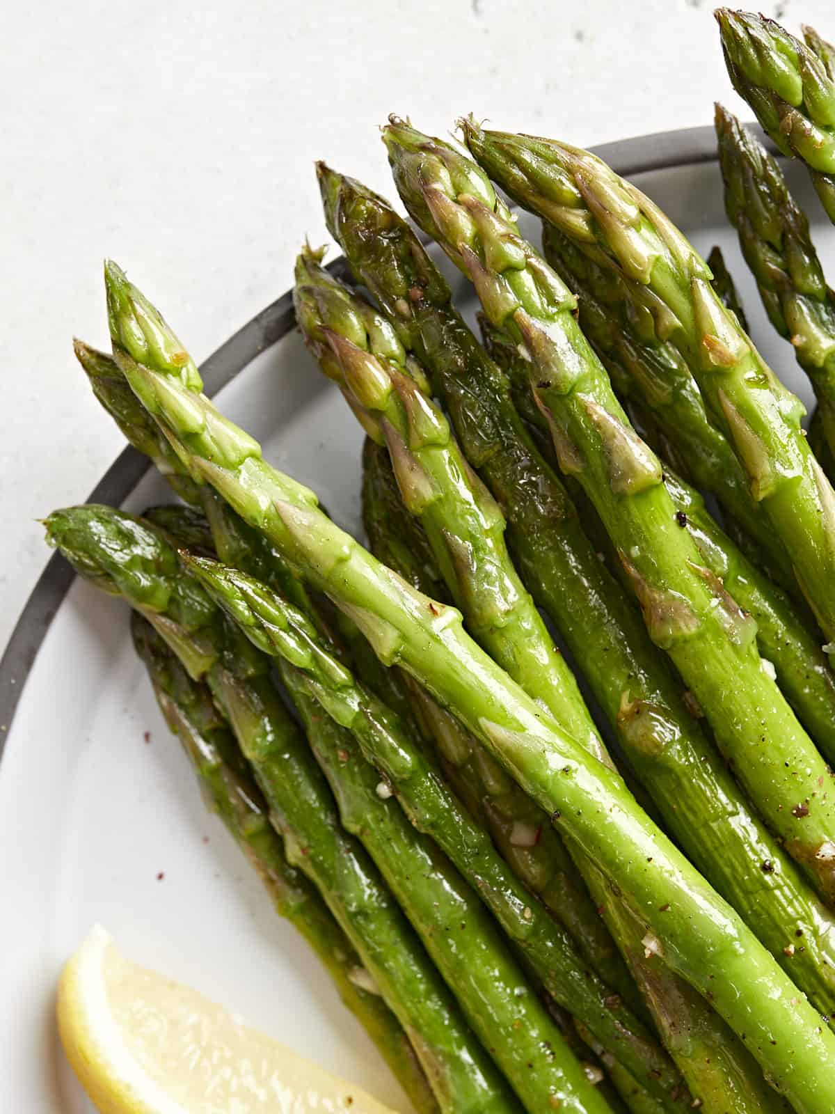 close up of sauteed asparagus tips on a plate with a lemon wedge.