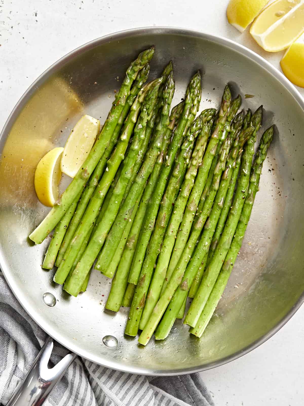 overhead view of sauteed asparagus in a frying pan with lemon wedges.