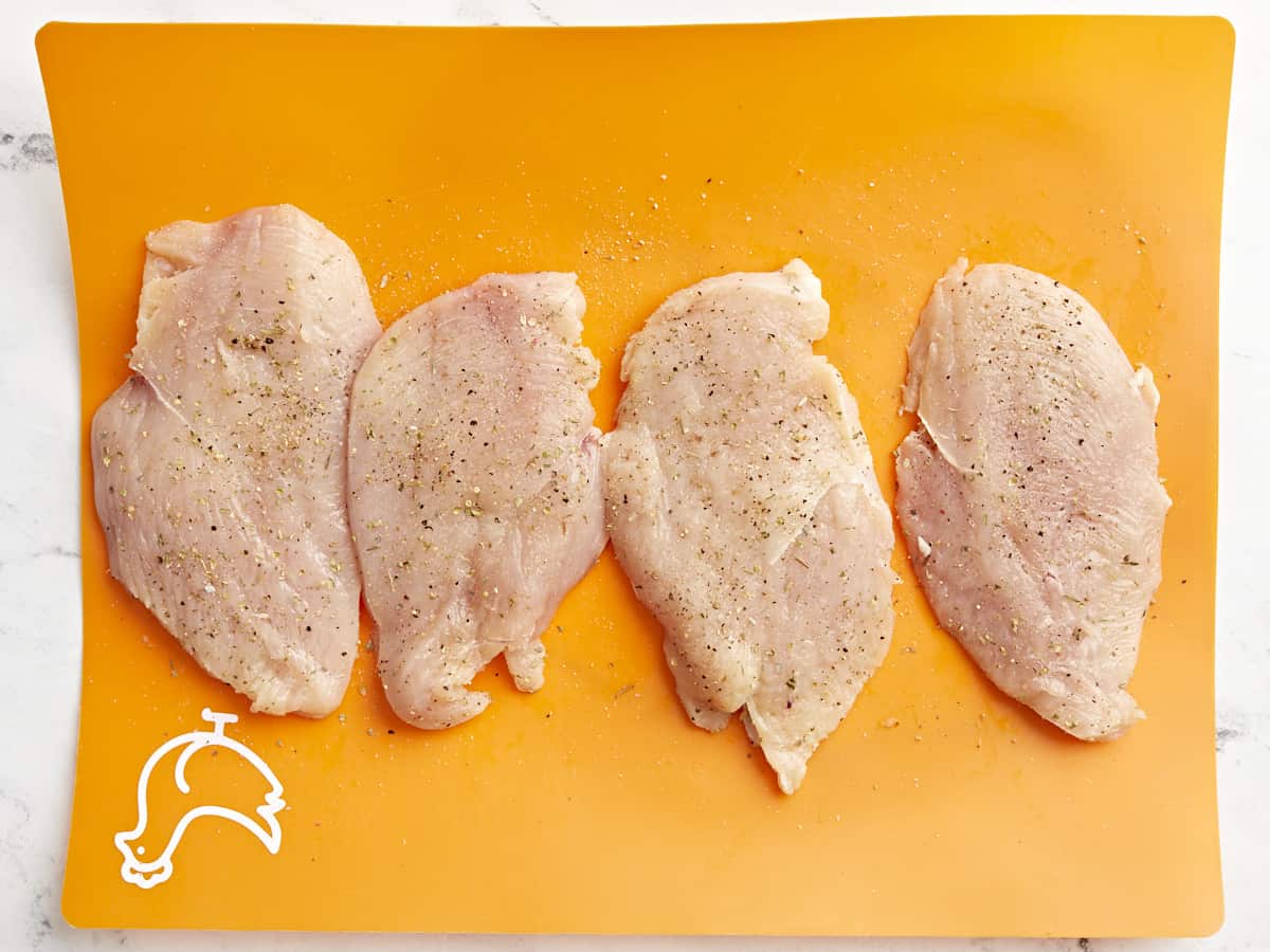 4 seasoned chicken breasts on an orange cutting board.